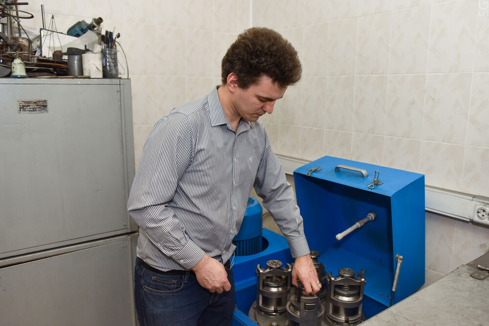 На изображении показан сотрудник Центра, взаимодействующий с оборудованием синего цвета, которое может быть частью установки для синтеза или обработки материалов.